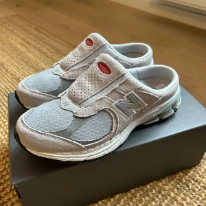 New Balance 2002 mules gråa - Helt nya, supersnygga och trendiga mules från New Balance. Jättesköna men tyvärr lite för små för mig som vanligtvis är en 38, så tror de bäst passar en 37-37,5.   Helt nya och oanvända, endast testade inomhus.   Nypris ca 1400kr