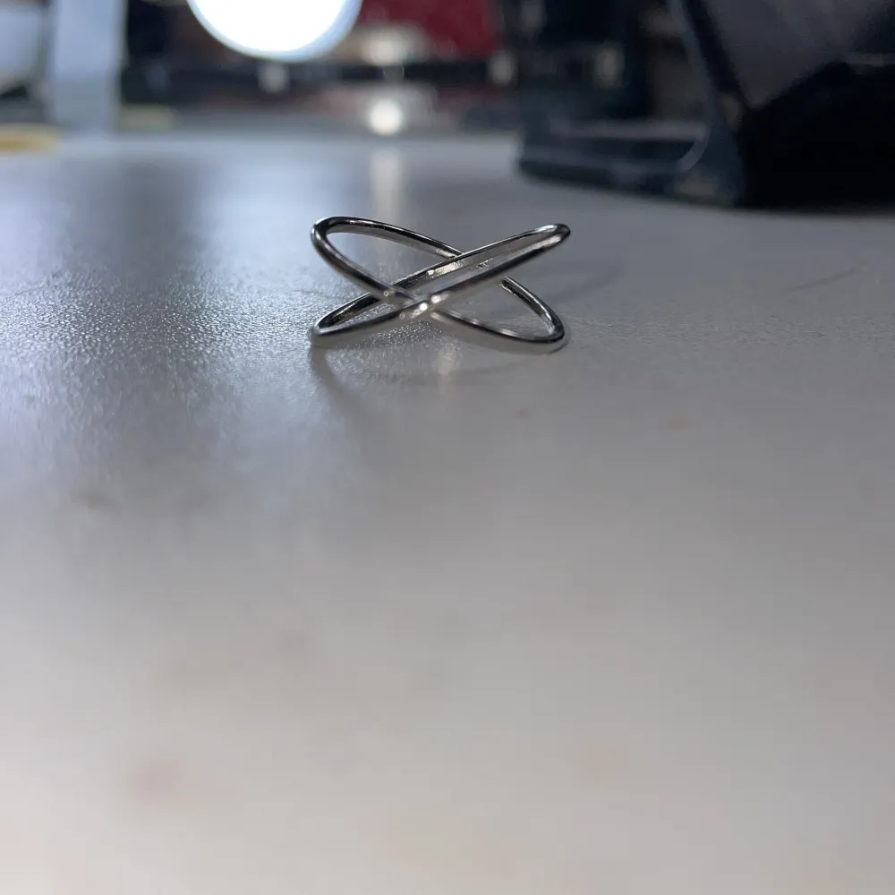 En silver ring som är format som ett kryss. Accessoarer.
