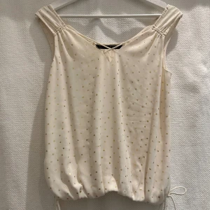  Remefärgad topp med guld från Zara - Cremefärgad top med guldprickar från Zara.   Bred resår nedtill samt rynkad längst ner i sidorna med knytband.   Strl. S