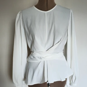 Blus - Oanvänd vit blus med knytdetalj som går att ha bakåt eller framåt. Passar S/liten M