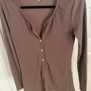 Långärmad topp fårn Nelly - Brun långärmad ropp från Nelly (Nellytrend) med tre knappar, storlek S. Nyskick, anvönd nån enstaka gång.