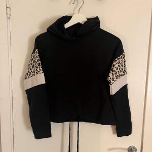 Svart hoodie med leopardmönster på ärmarna, huva och snöre så att man kan dra åt längst ner på tröjan. Nyskick
