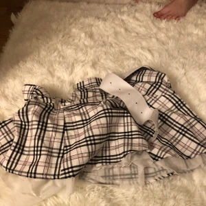 En svart vit rosa rutig kjol - En svart vit rosa rutig kjol medgett bälte till och lite volanger där nere