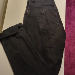 Jeans - Svarta jeans med hål på knäna. Uppvikta nere men går att vika ner om man vill. Midjan är 33cm och innerbenslängden är 74cm.
