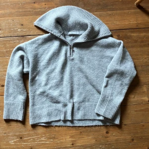 Grå stickad tröja från Bershka - En mysig och bekväm grå stickad tröja från Bershka. Tröjan har en hög krage med dragkedja och ribbstickade detaljer vid kragen, ärmsluten och nederkanten. Perfekt för kyliga dagar eller lite kallare sommarkvällar. Använd sparsamt så i fin kvalite! Skicka dm vid frågor.