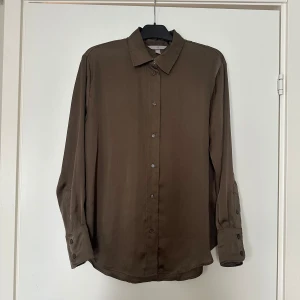 Beige blus - En beige blus i blankt material. Knappt använd.