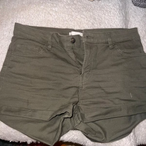 Olivgröna shorts från H&M - Ett par olivgröna shorts från H&M i storlek EUR 38. Shortsen har en knapp och dragkedja framtill, samt fickor både fram och bak. De är tillverkade i ett bomullsmaterial.