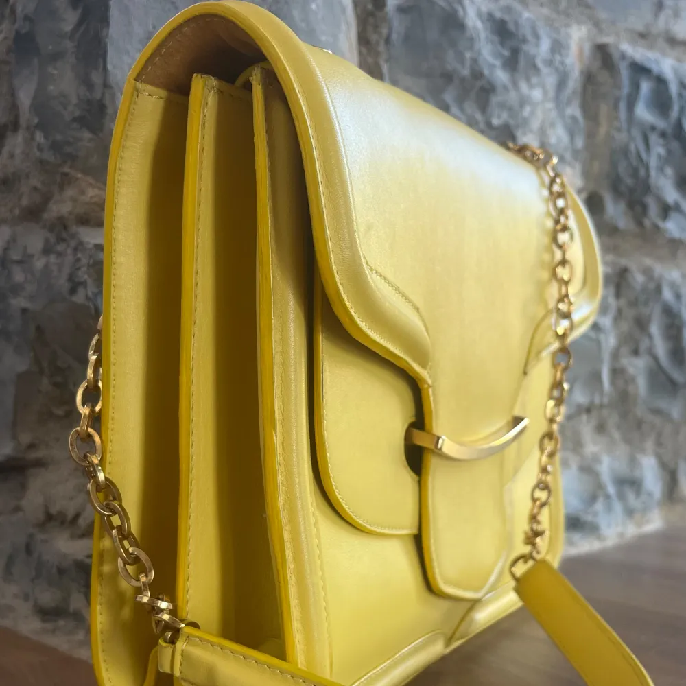 28 cm bred, 22 cm hög.  En äkta ALEXANDER MCQUEEN Calfskin Heroine Chain Satchel i Citrongul färg. Denna snygga shoulder bag är gjord i kalvskinns läder i gult. Guld länk shoulder strap och läder shoulder pad.  Köpt på Vestaire i Maj. Fläckar,se bild. Väskor.