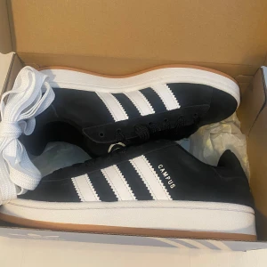 Nya svarta Campus 00s j 38 - Adidas Originals Campus 00 s j 38 Svarta (Core Black/Cloud White/Cloud White) Ingår både vita och svarta skosnören.  Nya och oanvända. Ligger kvar i kartong.  Köpta i svensk webbutik och kommer inte från någon massimport utomlands.