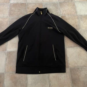 Hugo boss zip - En svart snygg hugo boss zip med guldiga detaljer. 9/10 skick. Inga problem med den alls. Perfekt till sommarkvällar då den är lite tunnare i materialet men fortfarande jätteskön. Priset kan diskuteras vid snabb affär!