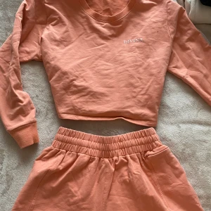 Träningsset - Träningsset från Divina. I korall/orange färg. Tröjan är cropped men långärmad. Shortsen är highwaisted och har ficka med dragkedja (perfekt för mobiltelefon). Materialet är av mjukt bomull som andas. Har använt de en gång. Båda är i storlek S.