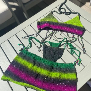 Hand gjort festival set - Multifärgad, glittrig Stickat set med micro bralette, högmidjad stringtrosa och en micro kjol. Garnet är tunt,stretchigt! Och har lila tinsel som glittrar. Handsydda pärlor på. Toppen & trosan är sjusterbara med knytning. Helt oanvänd,endast foto