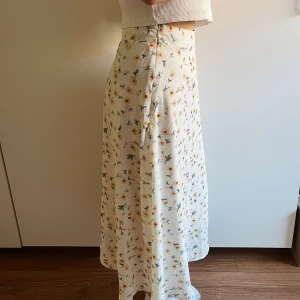 Sommrig Långkjol - Säljer nu en gammal favvis som är i otroligt bra kvalite och knäpps med hjälp av dragskedja på sidan. Den slutar lite ovanför anklarna på mig och är superfin med ett par converse exempelvis. Den har en varm vit färg med gula blommor.