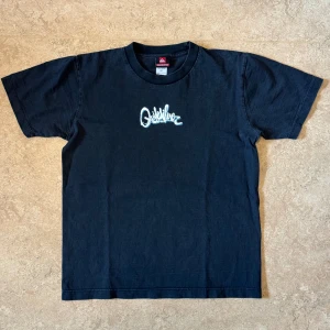 Vintage Quicksilver Svart T-Shirt - Quicksilver T-Shirt med tryck både fram och bak, finns cracking i trycket. Storlek: M, Armhåla till armhåla: 47 cm Längd: 60 cm