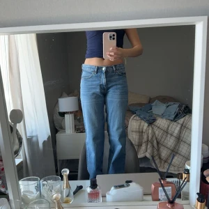 Blå jeansbyxor - Ett par blå jeansbyxor med hög midja och rak passform. Byxorna har en klassisk design med fem fickor och knappgylf.