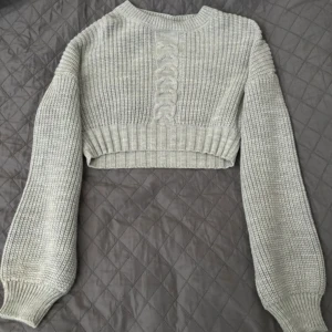 Grå stickad tröja från NA-KD - En oanvänd grå stickad tröja från NA-KD med ett flätmönster på framsidan. Tröjan är croppad med långa ärmar och ribbstickade muddar vid ärmslut och nederkant.💕