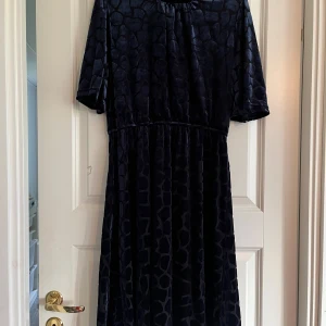 Mörk klänning med mönster - En mörkblå klänning med ett subtilt mönster. Klänningen har korta ärmar och en lös passform. Den är knälång och har en rund halsringning.