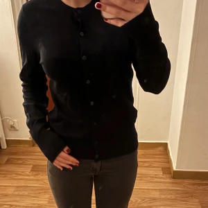 Svart cardigan med knappar, storlek XS 🖤 - Säljer en svart cardigan i storlek XS med knappar. Den är både elegant och mångsidig, perfekt för att komplettera din outfit. Cardiganen är i bra skick och redo för en ny ägare.