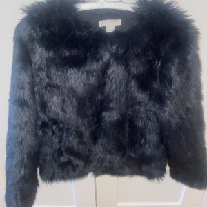 Svart pälsjacka från H&M - varm och tjock svart pälsjacka (inte äkta päls) från H&M. pälsjackan har en mjuk och fluffig textur med långa ärmar och en klassisk passform. Perfekt för kyliga dagar och kvällar.