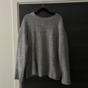 Grå stickad tröja - En grå stickad tröja med ett fint mönster. Tröjan har en rund halsringning och långa ärmar. Den är i en mjuk och skön kvalitet.