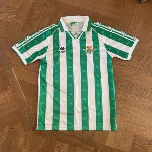 Real betis fotbollströja - En Real Betis tröja i utmärkt skick. Inga defekter alls då den knappt används. Den är i storlek M men passar även S enligt mig. Har du några som helt frågor så är det bara att skriva!😇
