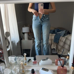 Blå jeans med knappar - Ett par blå jeans med hög midja och knappar framtill. Jeansen har en bootcut-stil och är i bra skick.