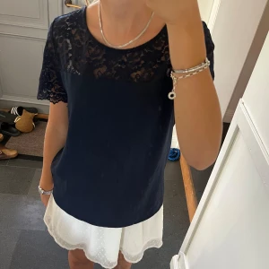 Mörkblå spetstopp - Mörkblå kortärmad tröja med spets från Vila i storlek 38, passar S och M. Lite nopprig men annars fint skick. Säljer även kjolen. Använd gärna köp nu!