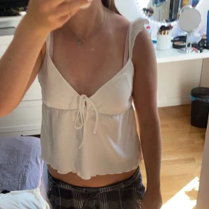 Vit linne topp - En vit linne topp med smala axelband och knytning framtill. Toppen är ärmlös och har en lös passform.