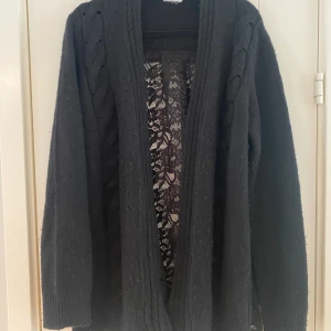 Svart öppen kofta med spets på baksidan i strl L från Liu Jo - Svart öppen kofta med spets på baksidan i strl L från Liu Jo. Lappen med strl är bortklippt men jag vill minnas att det är en strl L. Dubbelkolla måtten nedan.  Mått Över bröstet: ca 67 cm Längd från axeln: ca 76 cm  Koftan är lite nopprig.