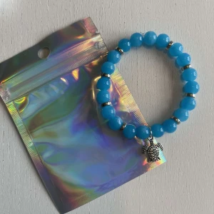 Egengjort pärlarmband  - Egengjort pärlarmband med blåa och silvriga pärlor. Armbandet har en berlock som avbildar en sköldpadda. 