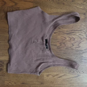 Brunt linne - En brun kort topp med 2 knappar som går att knäppa upp. Köpt från Bikbok och i storlek S.