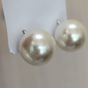 Pärlörhängen - Ett par eleganta pärlörhängen med en glänsande vit yta. Örhängena har en klassisk design med en rund form och är fästa med stift och bakstycken i metall.