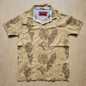 Vintage tröja med mönster - Grymt cool retro t-shirt / piké med gulbeige bas och brunt mönster samt krage. I nyskick, även om den är köpt vintage. Storlek: L Mått skickas på begäran, svarar på alla frågor.