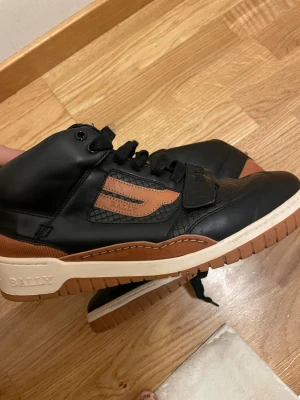 Svarta och bruna sneakers från Bally - Snygga high-top sneakers från Bally i svart  . Perfekta för dig som gillar streetstyle och premiumkänsla. Använda endast en gång och helt slutsålda överallt