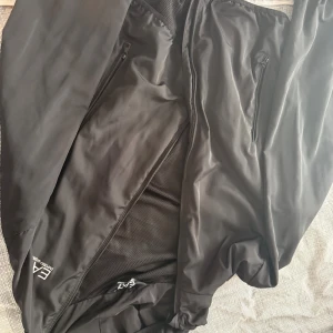 Svart vindjacka från EA7 Emporio Armani - Snygg svart vindjacka från EA7 Emporio Armani med dragkedja och två fickor framtill. Jackan har meshfoder på insidan och logga på bröstet. Perfekt för dig som vill ha en stilren och sportig look.