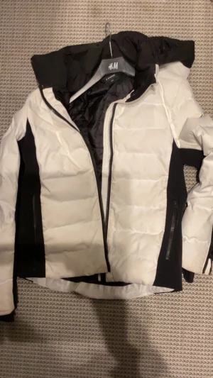 Vit och svart pufferjacka från Everest - Snygg pufferjacka från Everest i vit och svart med dragkedja framtill och två sidofickor med dragkedja. Jackan har hög krage och är perfekt för kalla dagar. Materialet är syntet och jackan har en modern, sportig look.