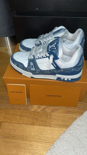 Louis Vuitton blå/vita sneakers - Exklusiva Louis Vuitton sneakers i blått och vitt med klassiskt monogrammönster. Skorna har snörning, rund tå och platt sula. Ovandelen är i en mix av skinn och textil med tydliga LV-detaljer och logga på tungan. Perfekta för dig som vill sticka ut med lyxig streetstyle.