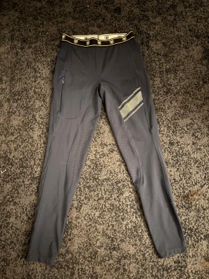 Mörkblåa tighta ridleggings - Säljer ett par mörkblåa ridleggings från hööks med hög midja och elastisk logotypmönstrad linning. Endast använda 1 ridpass. Byxorna har silikonmönster för extra grepp, en ficka med dragkedja och snygga detaljer i vitt på låret. Perfekta för dig som vill ha stil och funktion i stallet. STR M. Hör av dig via E-mejl eller mobil då jag inte kan ta emot Swish på detta nmr. Pris 500 kr varav ord pris är 650.  E-mejl emli.com@icloud.com mobil-0728875624 MVH Emilia/marina😊