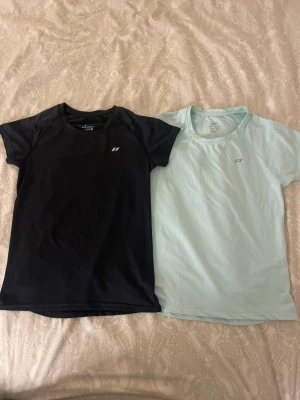 Två kortärmade tränings-tshirts från Pro Touch - Säljer två snygga tränings-tshirts från Pro Touch , en i svart och en i ljusblå. Båda har rund hals, korta ärmar och reflekterande detalj på ryggen. Materialet är lätt polyester som andas och passar perfekt för aktiva dagar. Diskret logga framtill. Jag tror att dom är oanvända men är inte helt säker. Säljer båda för 50kr