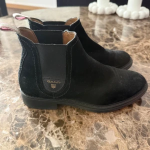 Svarta chelsea boots från Gant - Snygga svarta chelsea boots från Gant i mocka med klassisk rund tå och elastiska paneler på sidorna. Skorna har låg klack och en diskret logga på sidan. Perfekta för dig som vill ha en stilren och tidlös look.