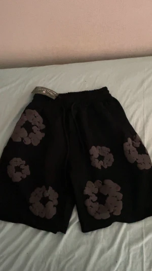 Svarta shorts från Denim Tears - Svarta shorts från Denim Tears med gråa blommiga tryck över hela plagget. Modellen