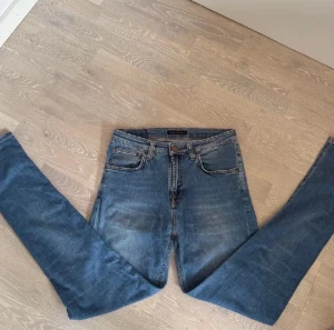Nudie Jeans - Säljer ett par klassiska blå skinny jeans från Nudie Jeans med hög midja. Jeansen har fem fickor, orangea sömmar och Nudie-logga på bakfickan. Tillverkade i mjukt denimtyg med snygg tvättad look och raka ben.