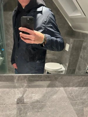 Mörkblå vindjacka med knappar - Snygg mörkblå vindjacka med klassisk krage och tryckknappar framtill. Riktigt bra skick på jackan. Jag på bilden är 188cn och bär storlek M. Hör av er vid funderingar:)