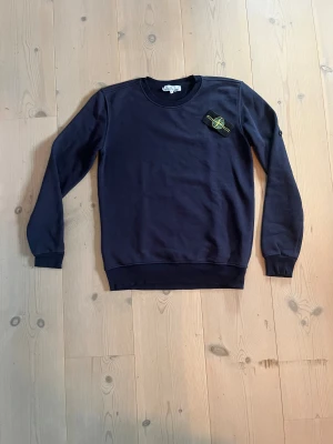 Mörkblå Stone Island sweatshirt S - Säljer en mörkblå sweatshirt från Stone Island i storlek S. Tröjan har klassisk rund hals, ribbade muddar och den ikoniska Stone Island patchen på vänster ärm. Materialet är mjuk bomull och passformen är normal. Perfekt för dig som gillar streetwear och snygga detaljer.