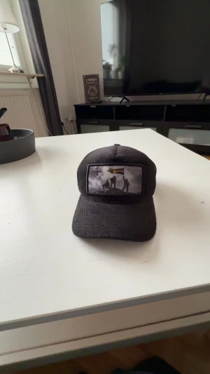 Svart truckerkeps från Revenite - Svart truckerkeps från Revenite med mesh på sidorna och justerbar snapback. Framtill finns en patch med motiv av soldater och svensk flagga. Kepsen har böjd skärm och coolt tryck som sticker ut. Perfekt för dig som gillar streetstyle och vill ha något unikt.