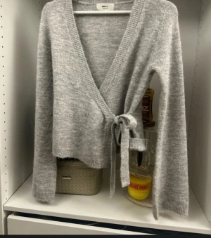 Grå omlottkofta med knyt - Supermysig grå omlottkofta från Gina Tricot med knyt i sidan och djup v-ringning. Koftan är stickad och har långa ärmar med ribbade muddar. Perfekt att slänga på sig när du vill ha en chill och snygg look.