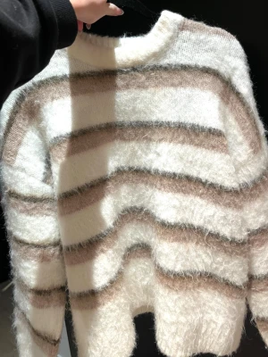 Randig fluffig stickad tröja - Mysig stickad tröja med breda ränder i vitt, beige och brunt. Tröjan har en rund hals och långärmade ärmar, och är gjord i ett fluffigt material som känns extra skönt. Perfekt för dig som gillar en chill och trendig look.