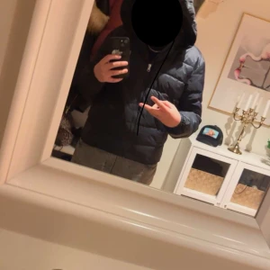 Svart pufferjacka från Gant med huva - Säljer en svart pufferjacka från Gant med huva och dragkedja framtill. Jackan har Gant-logga på bröstet och är vadderad för extra värme. Perfekt för kyliga dagar och har en clean, sportig look.