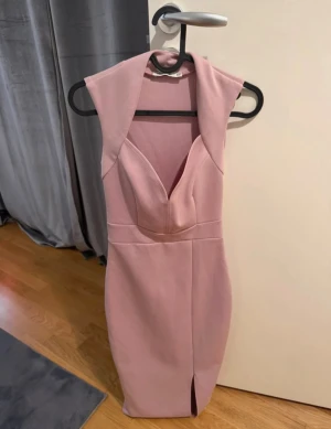 Ljusrosa långklänning med slits - Supersnygg ljusrosa långklänning med v-ringning och markerad midja. Klänningen är ärmlös och har en liten slits framtill för extra edge. Sitter tight och har en stilren, elegant look som verkligen sticker ut.