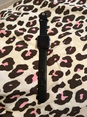 Apple Watch 42mm svart aluminium - Apple Watch 42mm med svart sportarmband och boett i mörkgrått aluminium (7000 series). Rektangulär skärm med digital krona på sidan. Stilren och modern design, perfekt för dig som gillar tech och vill ha koll på allt direkt på handleden.